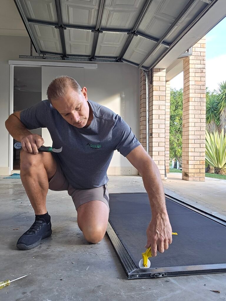 Handyman fitting a flyscreen door on a garage floor