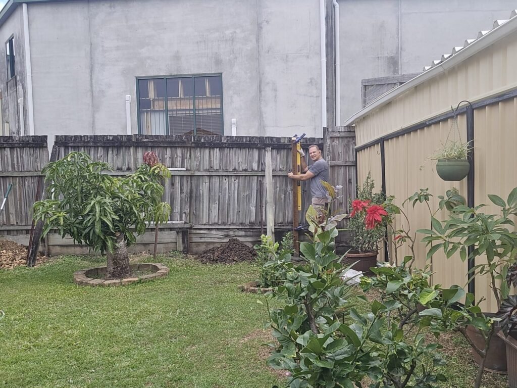 Before: Dan from SURVE plumbing a new fence post beside the old weathered fence